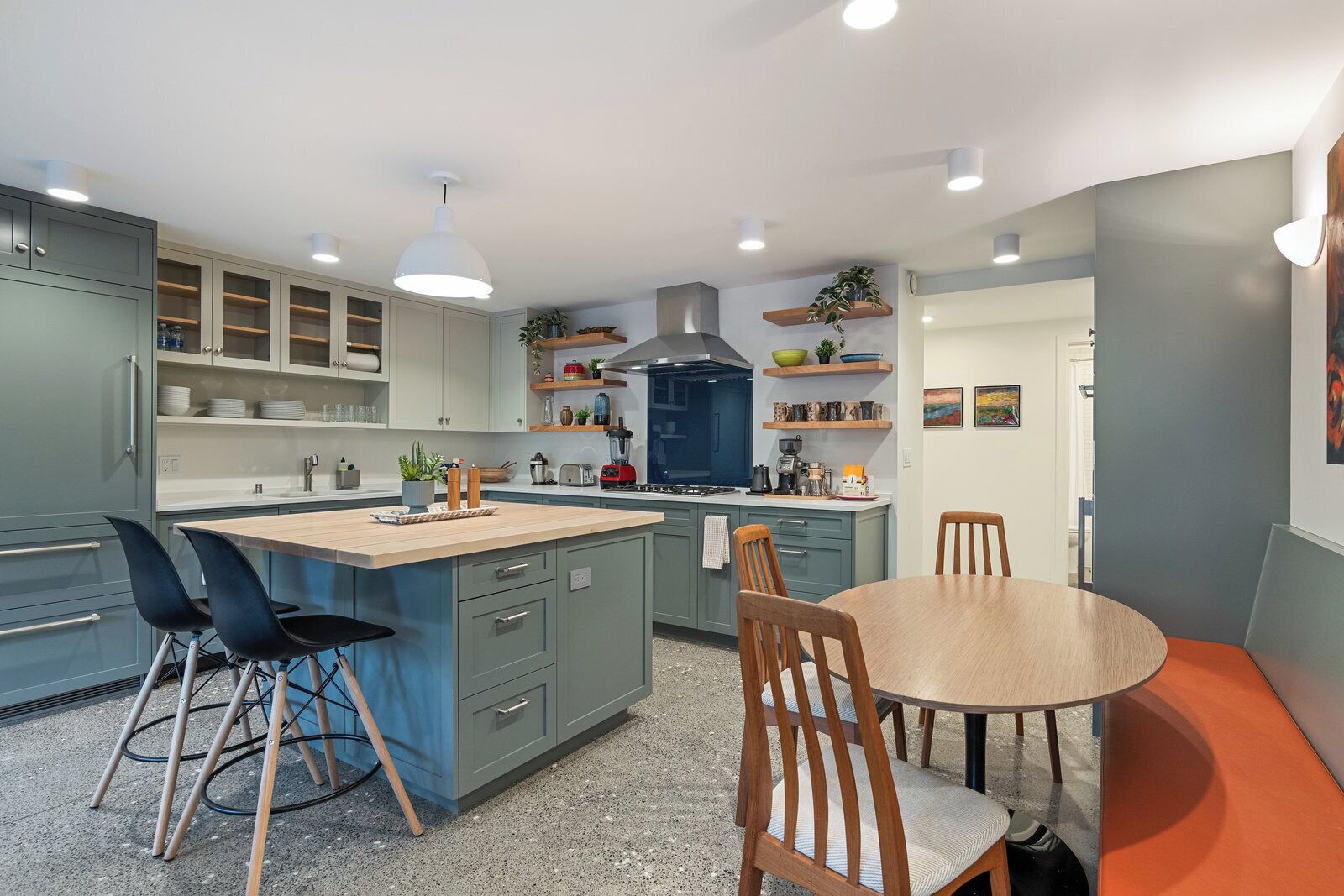 A modern kitchen with grey cabinets, a central island, and a dining area with a round table and chairs.