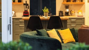 A modern kitchen with a dining area, featuring a sofa with cushions, a dining table, and various kitchen appliances.