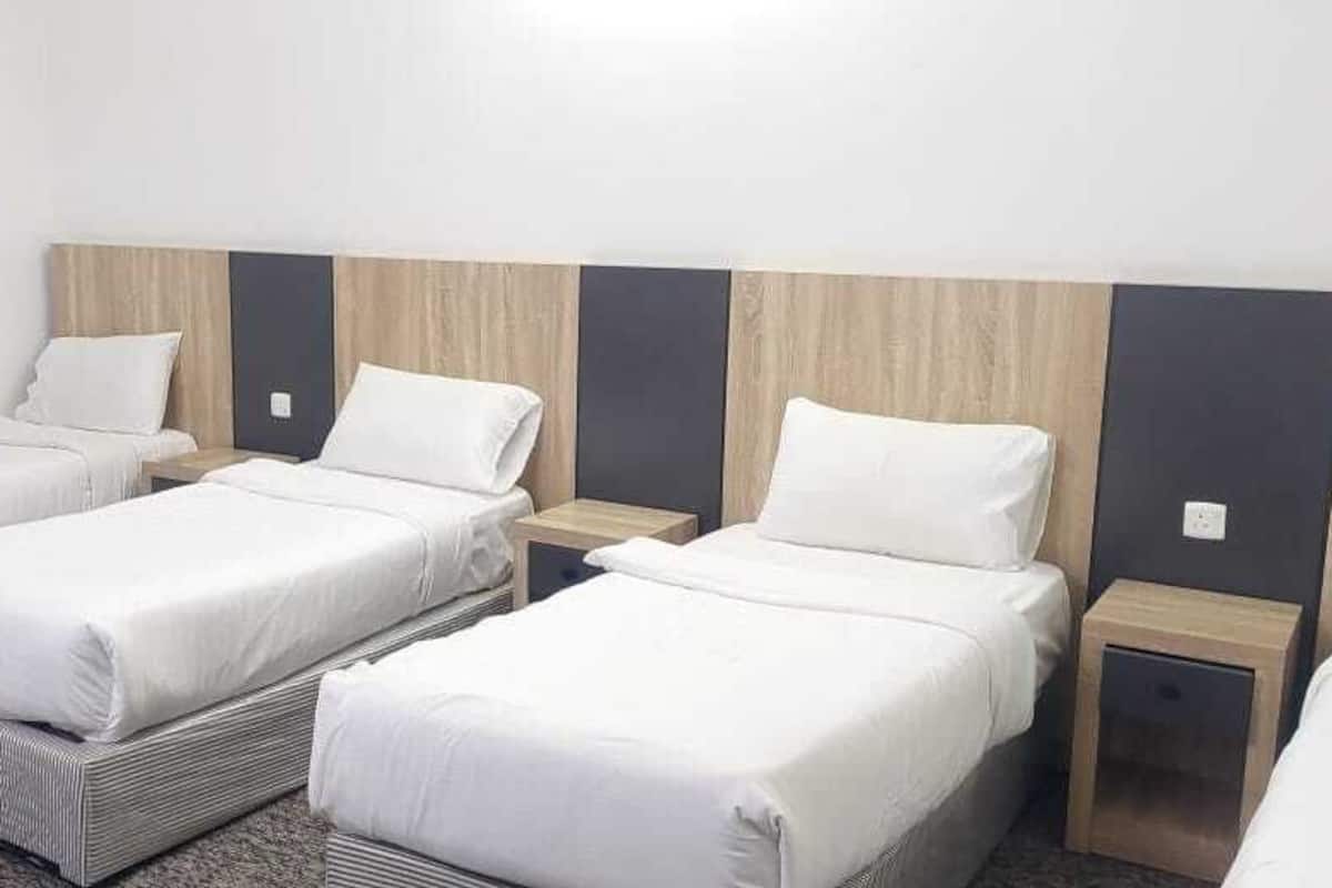 Une chambre d’hôtel avec trois lits simples, chacun doté d’une tête de lit en bois, de draps blancs et de tables de chevet.