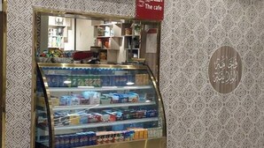 Ein Warenpräsentationskühlschrank mit verschiedenen verpackten Waren, eine Klimaanlage darüber und eine Wand mit Musterung sowie ein Schild, das ein Café anzeigt.