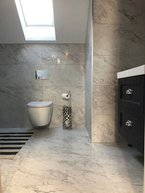 A modern bathroom with a skylight, marble tiles, a toilet, a toilet paper holder, and a black vanity. - Apartment Bushmills Hideaway, Parking,pets Allowed (Bushmills)