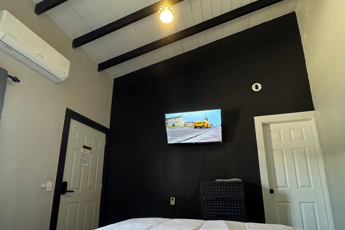 Habitación de hotel con una cama, televisión instalada en la pared y techo con vigas a la vista.