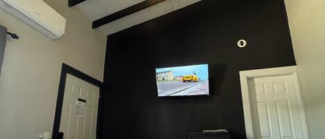 Una habitación con cama, televisor montado en la pared y techo con vigas a la vista.