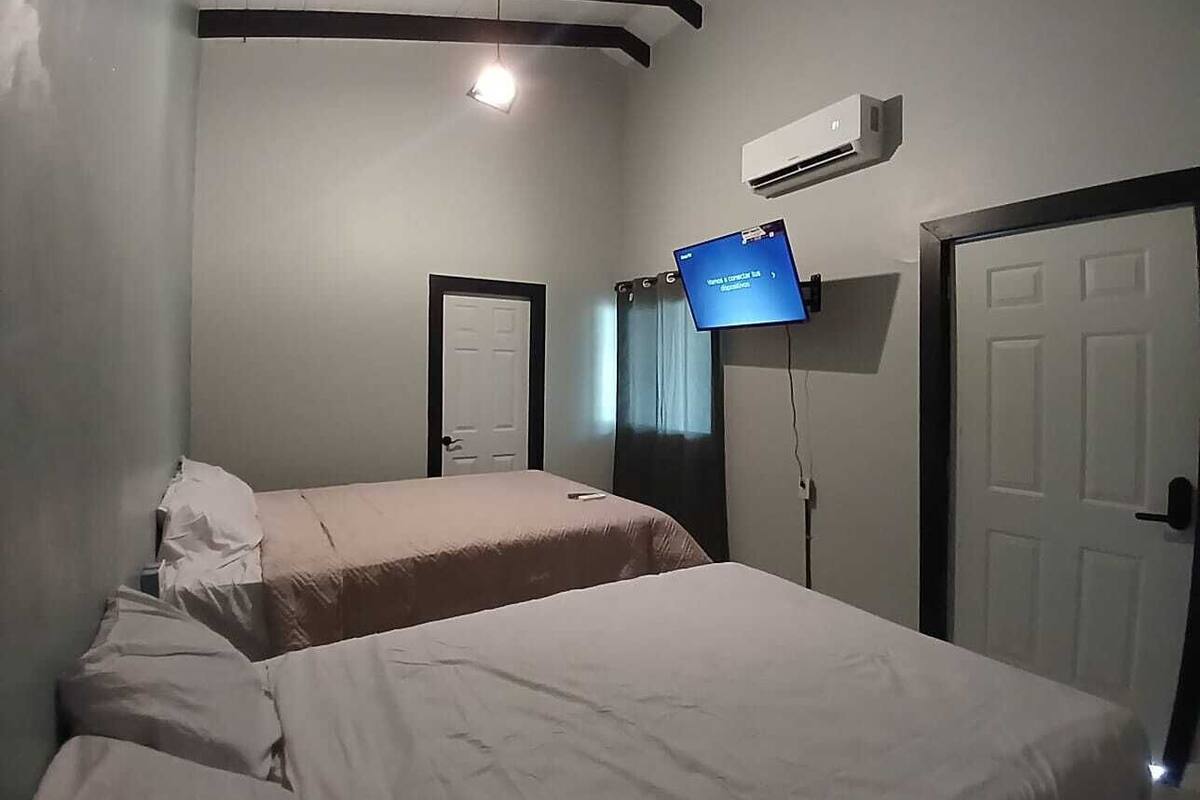 Una habitación de hotel con dos camas, un televisor montado en la pared y un equipo de aire acondicionado.