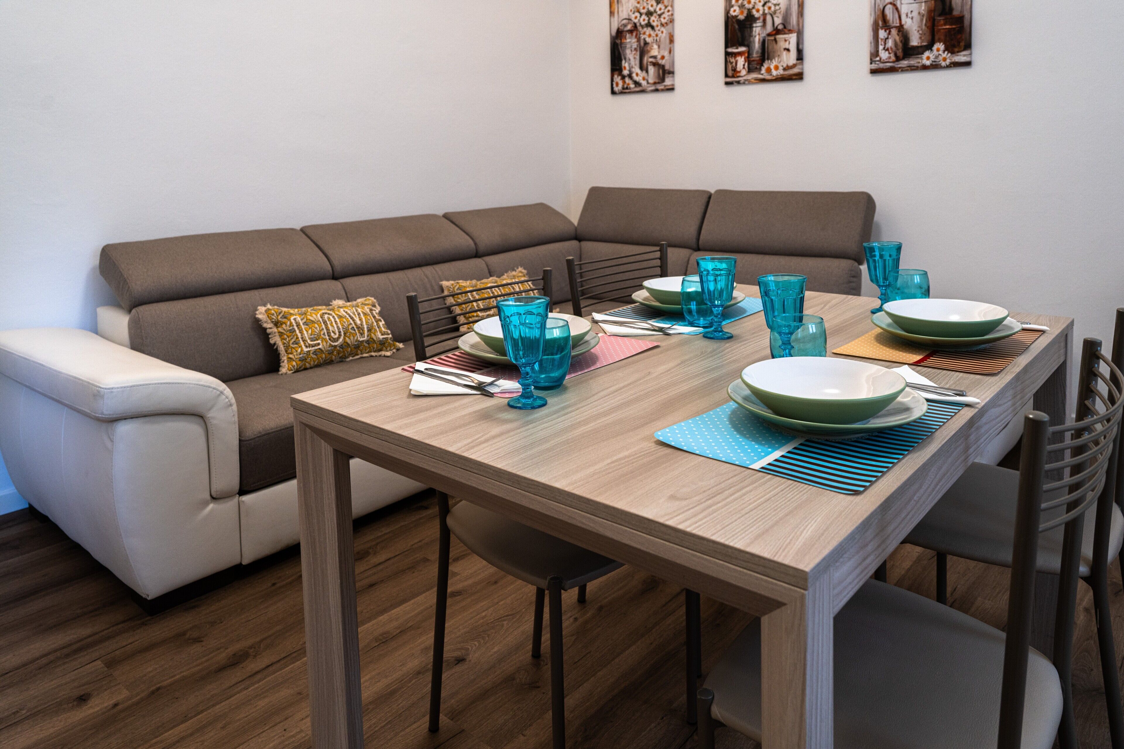 Un coin repas avec une table en bois dressée pour quatre personnes, un canapé marron et un fauteuil blanc.