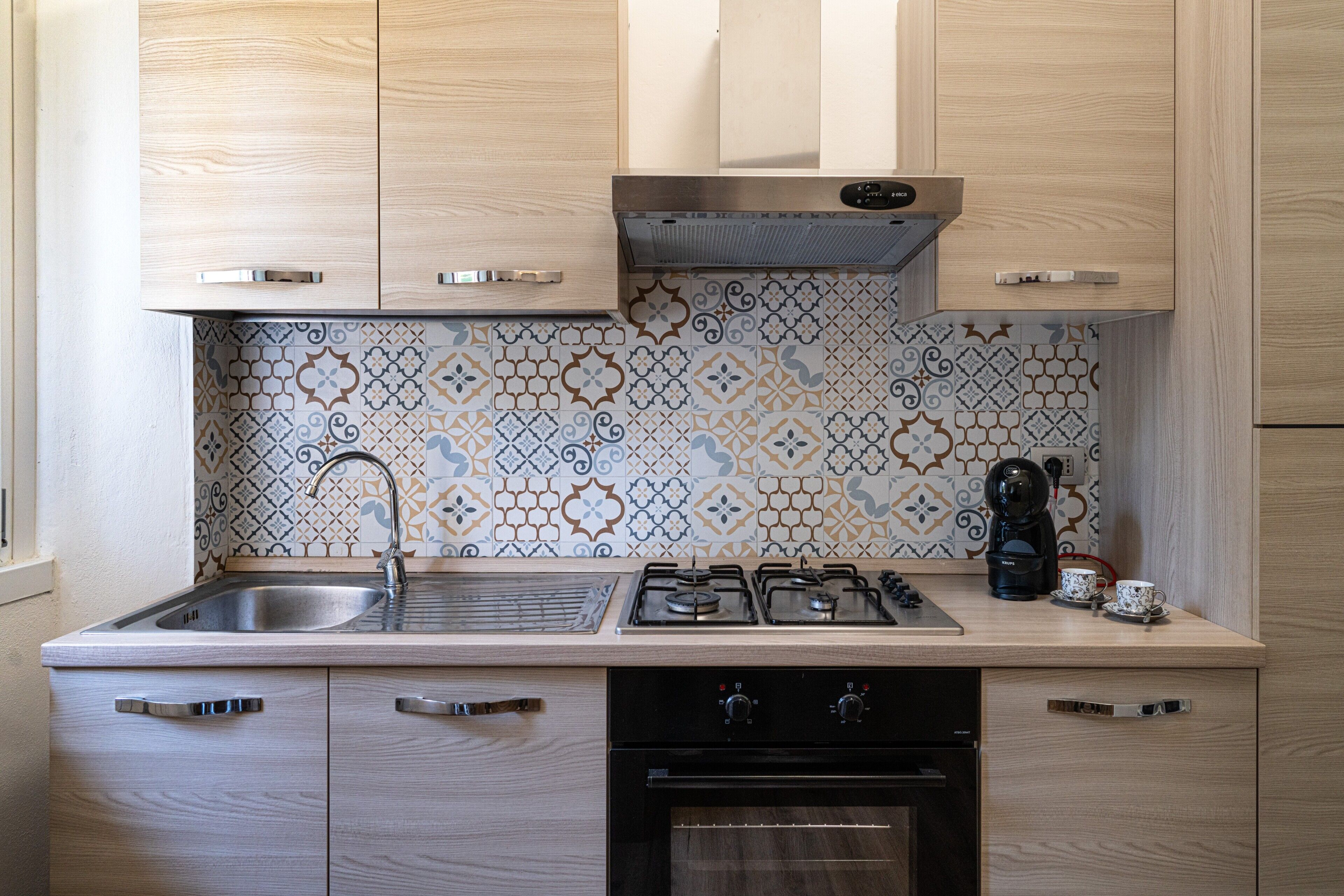 Una cucina con mobili in legno, piano cottura a gas, lavello e schienale decorato.