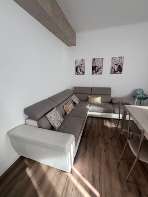 Un salon moderne avec un canapé d’angle gris, une petite table à manger et trois tableaux floraux accrochés au mur.