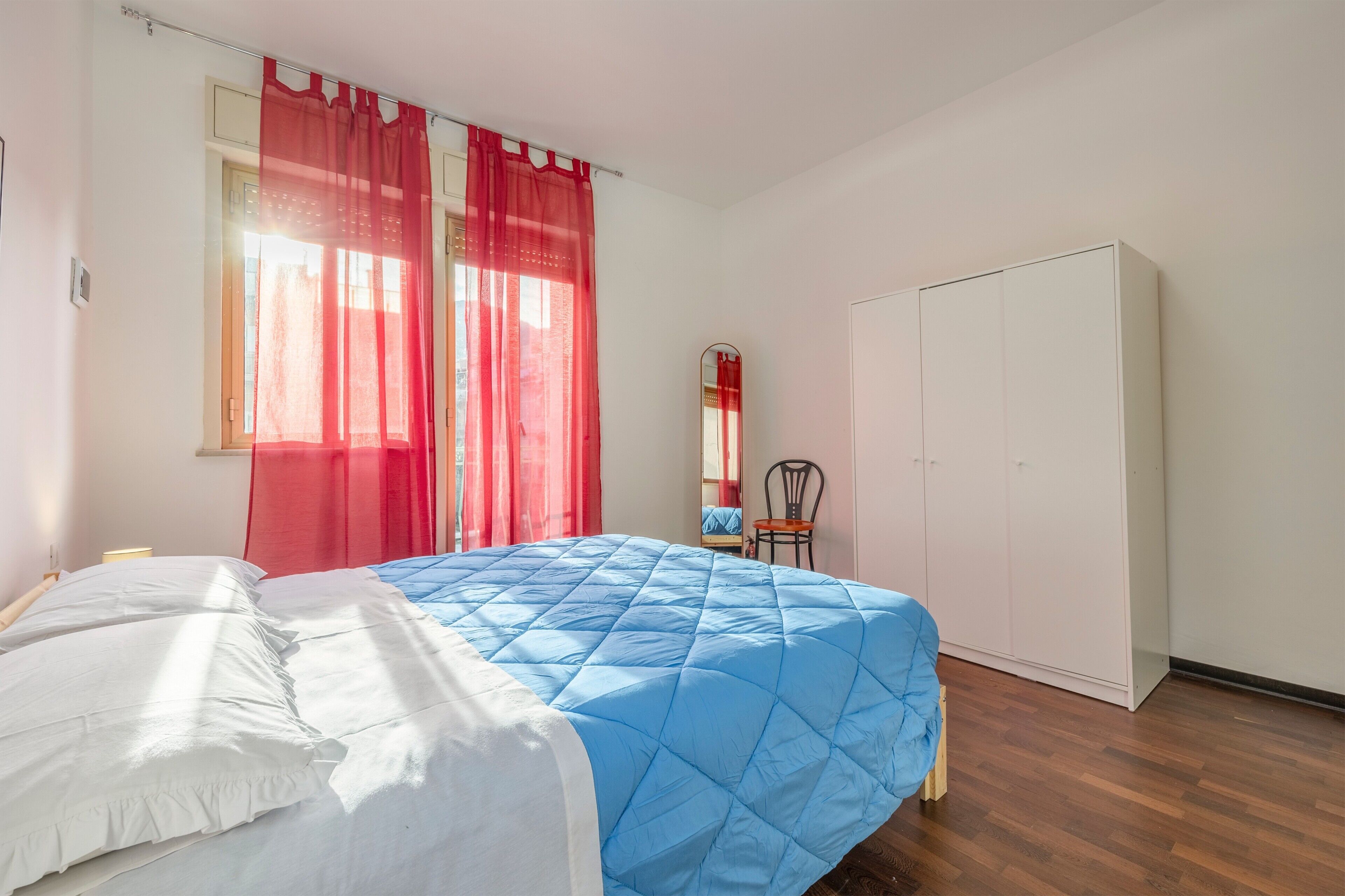 Une chambre à coucher avec un lit, une armoire, une chaise et une fenêtre avec des rideaux.