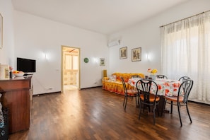 A room with a wooden floor, a dining table with chairs, a television, and a sofa.