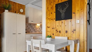 Une cuisine avec des murs recouverts de panneaux en bois, une table blanche avec des chaises et une horloge au mur.