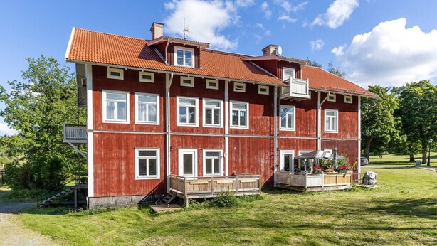 A large, red wooden building with multiple windows and a balcony, surrounded by a grassy area.