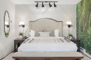 A bedroom with a large bed, two bedside tables, a bench, a mirror, and wall-mounted lamps.