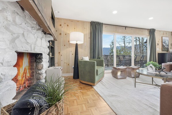 A cozy living room with a stone fireplace, comfortable seating, a large window, and a view of the outdoors.