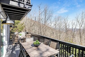 A wooden deck with a table and chairs, a potted plant, and a view of leafless trees.