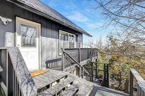 A two-story house with a wooden deck, a front door, and a staircase leading to the upper floor.