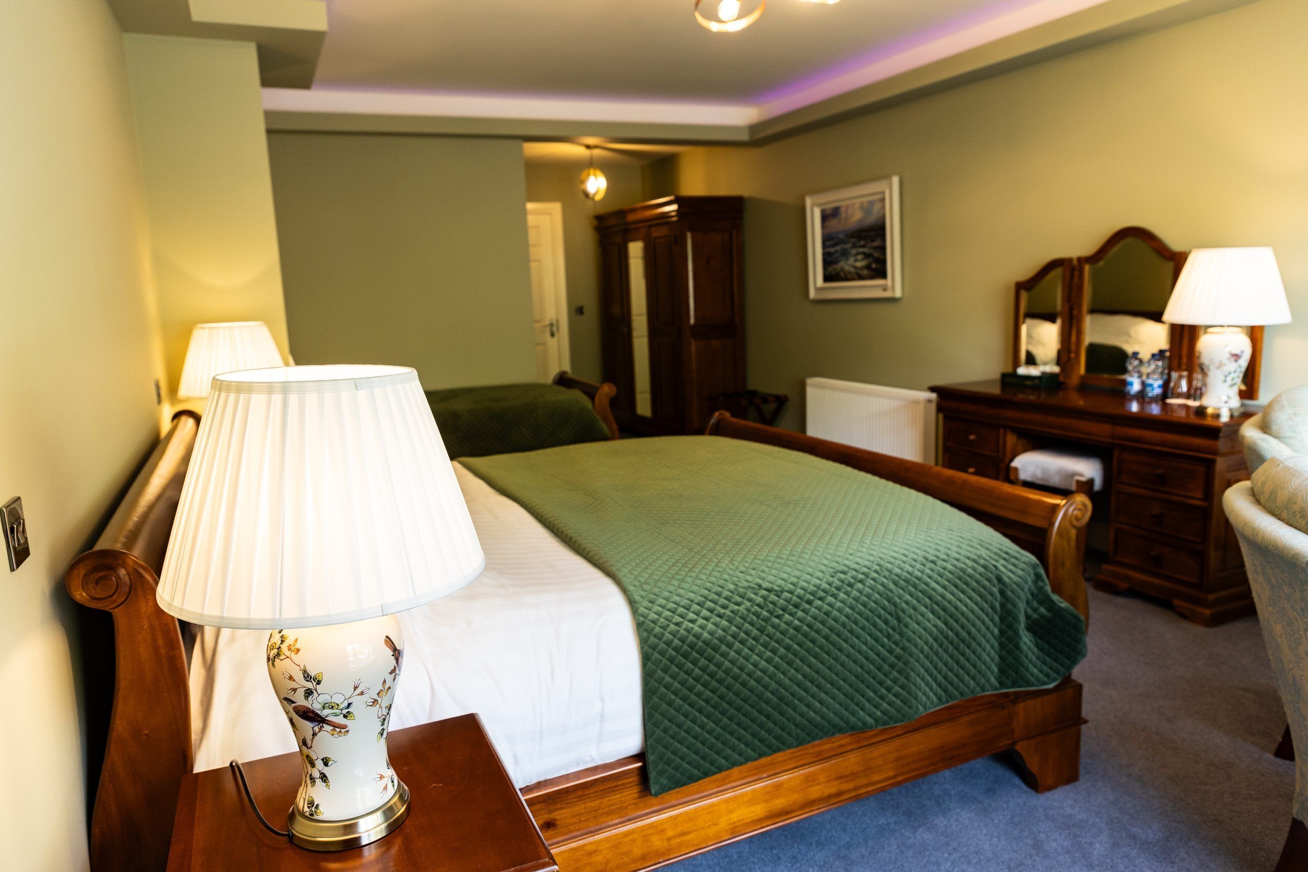 A neatly arranged bedroom with a bed, bedside lamps, a dresser, and a chair.