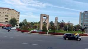 Un carrefour où se croisent des rues, agrémenté d’une sculpture moderne, d’une tour horloge et de bâtiments environnants.