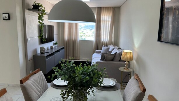 Una sala moderna con comedor, que incluye un sofá, un televisor montado en la pared, una mesa de comedor con platos y vasos, y un ventanal con cortinas.