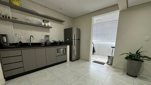 Una cocina moderna con armarios grises, un refrigerador de acero inoxidable y una encimera negra. Hay una planta en maceta y una ventana con persianas.