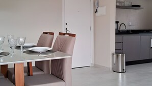 Un área de comedor moderna con una mesa de vidrio, cuatro sillas y un cubo de basura de acero inoxidable.