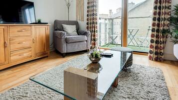A modern living room with a glass coffee table, a grey sofa, wooden cabinets, and a view of the outside.