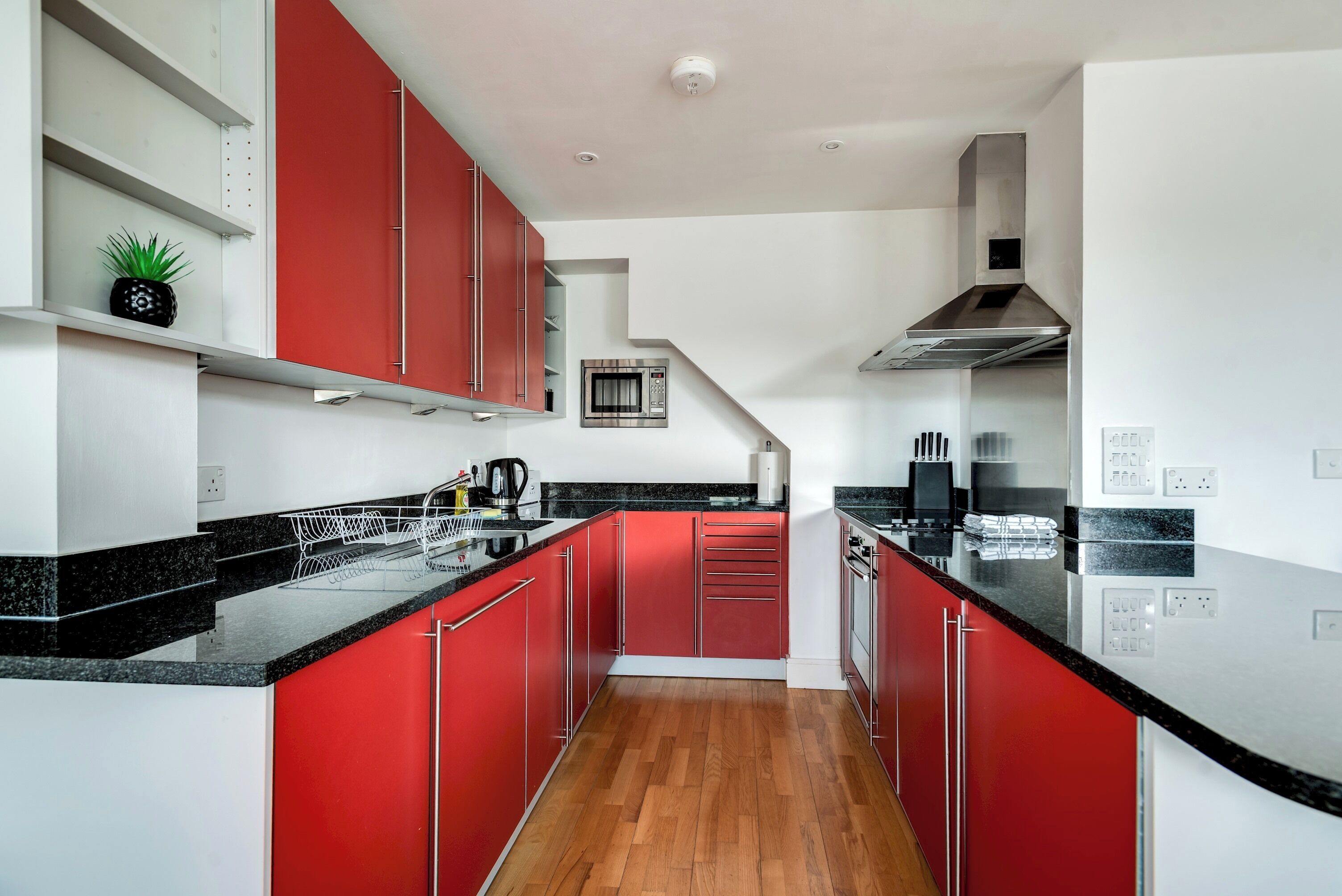 A modern kitchen with red cabinets, black countertops, and stainless steel appliances.