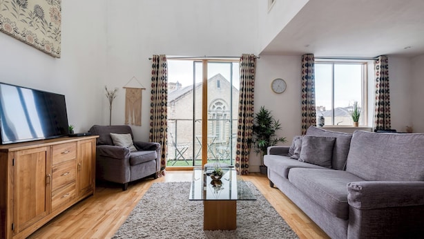 A modern living room with a grey sofa, a wooden cabinet, and a glass coffee table.