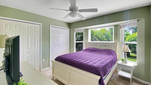 A bedroom with a bed, a ceiling fan, a desk with a computer, a lamp, and a window with a view of greenery. - Sunset Pines, Sleeps 6, heated pool, 2 Dog ok (Rotonda West)