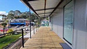 A covered balcony with a view of a commercial area, including a car dealership and a house with a Brazilian flag. -  Residencial Taulois Canela Centro (Canela)