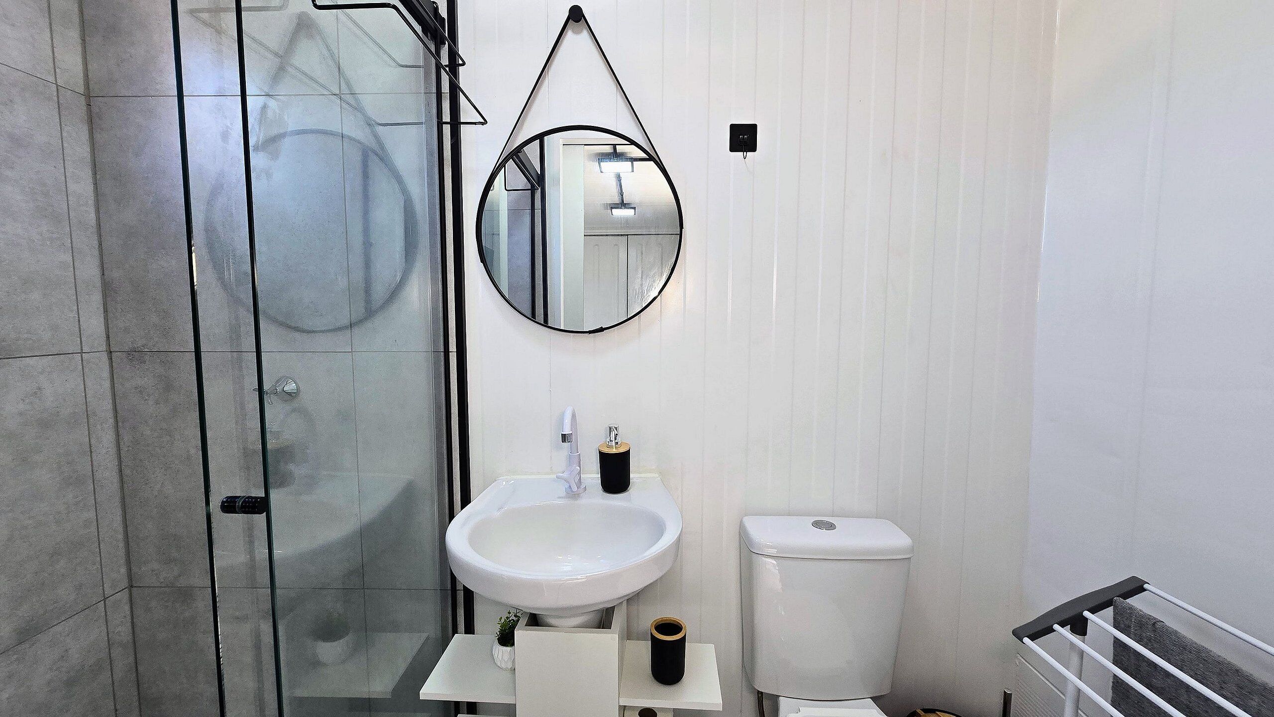 Un baño con cabina de ducha de vidrio, un lavabo blanco, un inodoro y un espejo con marco negro.