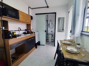 A compact kitchen with modern appliances, a dining area with a table set for two, and a view of the bathroom through an open door.