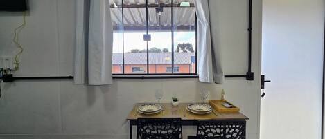 Un comedor con una mesa dispuesta para dos, una ventana con cortinas y vistas a un edificio.