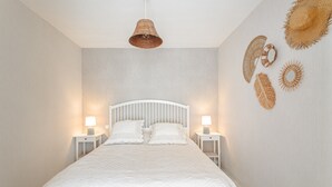 A bedroom with a white bed, two bedside tables with lamps, a woven ceiling light, and woven wall decorations.