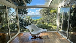 A modern room with large glass windows, a wooden floor, and a unique white chair. - GuestHost - Charming Pool Villa Porto Rotondo (Porto Rotondo)