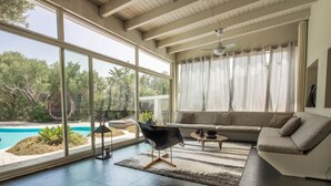 A modern living room with a large window, a pool, and a sofa. - GuestHost - Charming Pool Villa Porto Rotondo (Porto Rotondo)