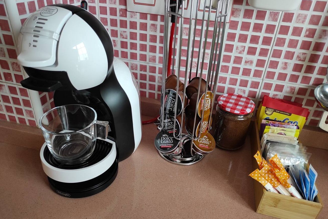Eine Küche mit Kaffeemaschine, einem Glas, einer Kaffeemühle, einem Vorratsglas und einer Packung Kaffeekapseln.