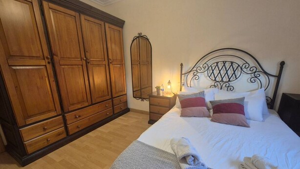 Um quarto com cama, guarda-roupa de madeira e um espelho.
