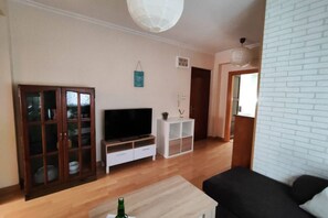 A living room with a television, wooden cabinet, white shelving unit, and a black sofa. - 1A164 via R2R, a 10-minute walk from Begoña Park (Gijón)