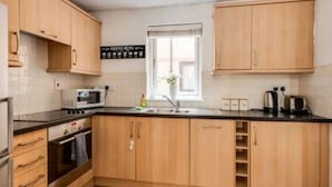 A modern kitchen with wooden cabinets, a built-in oven, a microwave, and a sink. - Central Oxford Oasis - Close to Colleges Shops (Oxford)