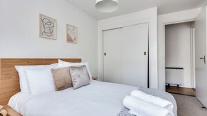 A neatly made bed with white linens and a wooden headboard, a white pendant light, and two framed artworks on the wall. - Central Oxford Oasis - Close to Colleges Shops (Oxford)
