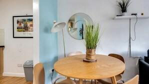 A dining area with a round wooden table, four chairs, a mirror, a framed picture, a potted plant, and a shelf with a plant and a camera. - Central Oxford Oasis - Close to Colleges Shops (Oxford)
