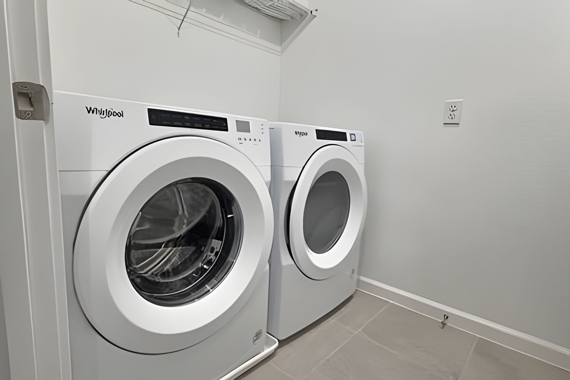 Two front-loading washing machines in a laundry room with a plain wall and a tiled floor.