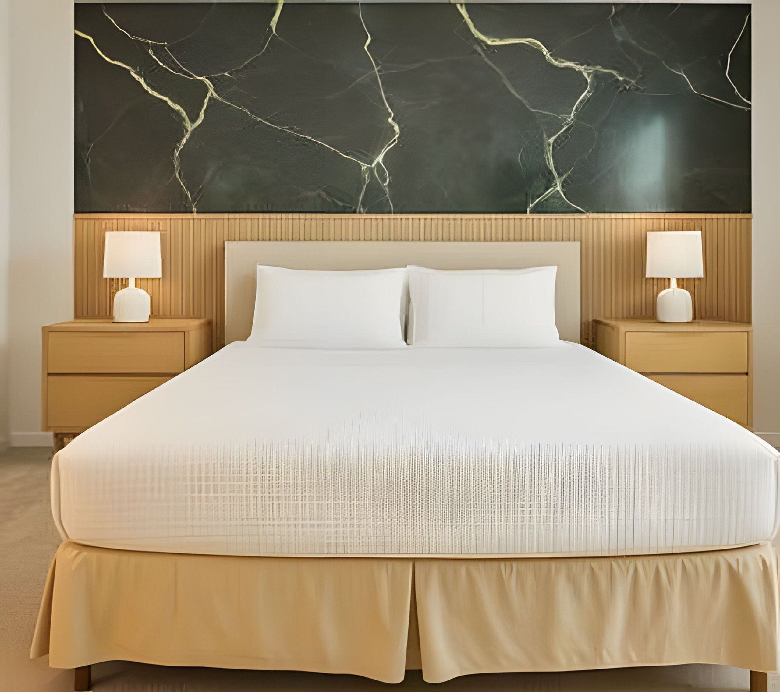 Un letto rifatto con lenzuola bianche, due comodini con lampade e una parete di grandi dimensioni con effetto marmo sopra il letto.