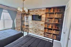 A bedroom with a brick wall, a bookshelf, a bed, and a TV mounted on the wall. - Modern 6BR Villa Heated Pool Solara Resort (Kissimmee)
