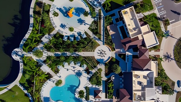 Vue aérienne d’un complexe hôtelier doté d’une piscine centrale, de plusieurs bâtiments et d’un environnement verdoyant.