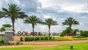 L’entrée d’un complexe hôtelier, avec des palmiers, un chemin de pierre et un panneau indiquant « SOLAR RESORT ».