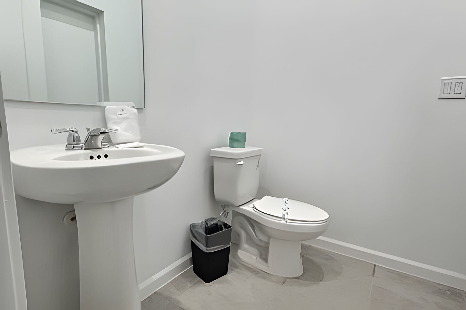 A bathroom with a white sink, toilet, and trash bin.