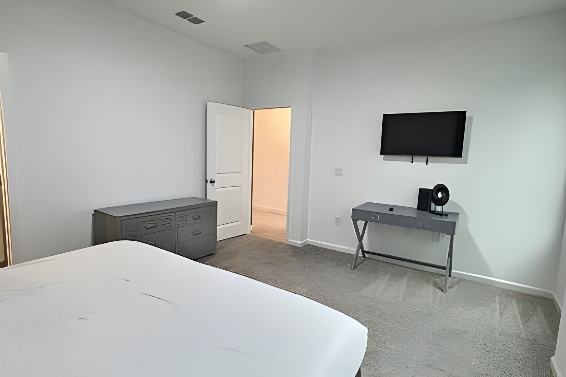 Een slaapkamer met een bed, een dressoir, een bureau met een computer en een televisie aan de muur.