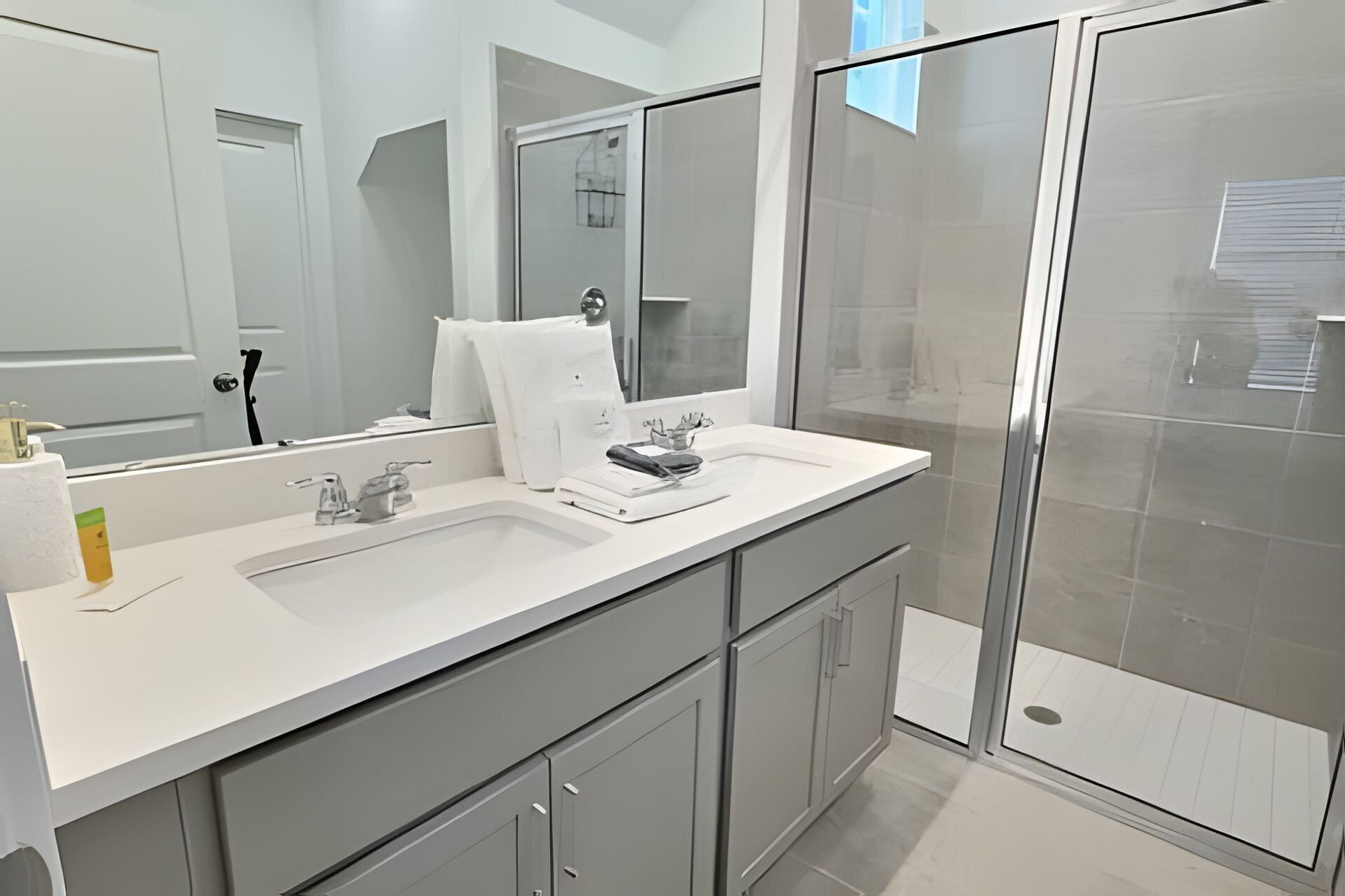 A modern bathroom with a large mirror, two sinks, and a shower area.