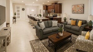 A modern living room with a grey sofa set, a coffee table, and a dining area with a long table and chairs. - 3bd/3.5ba Retreat With Private Pool Solara Resort (Kissimmee)